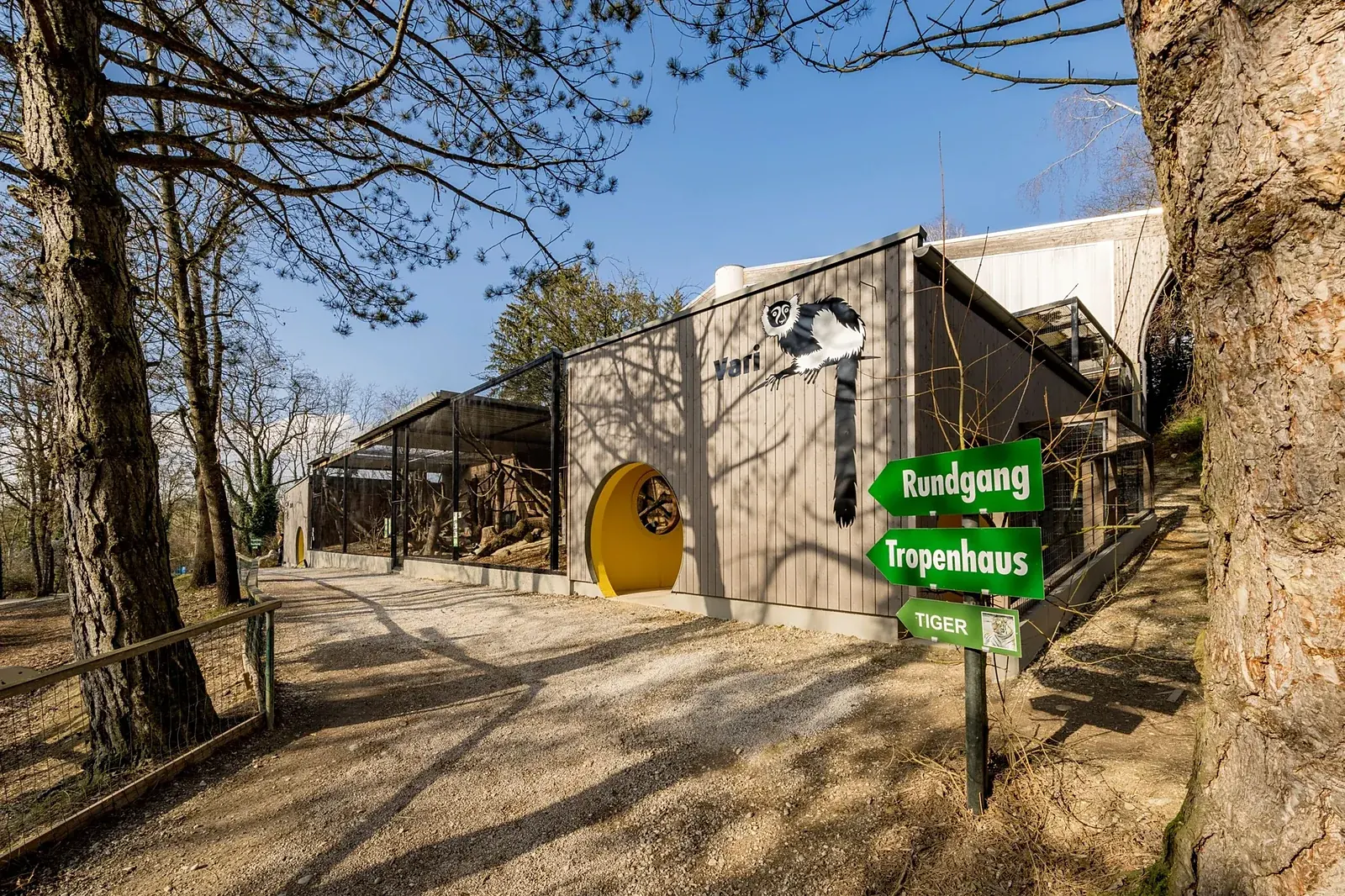 Katta-Anlage im Zoo Schmiding – Holzfassade mit runden grün gefassten Öffnungen und geschwungenem Dach