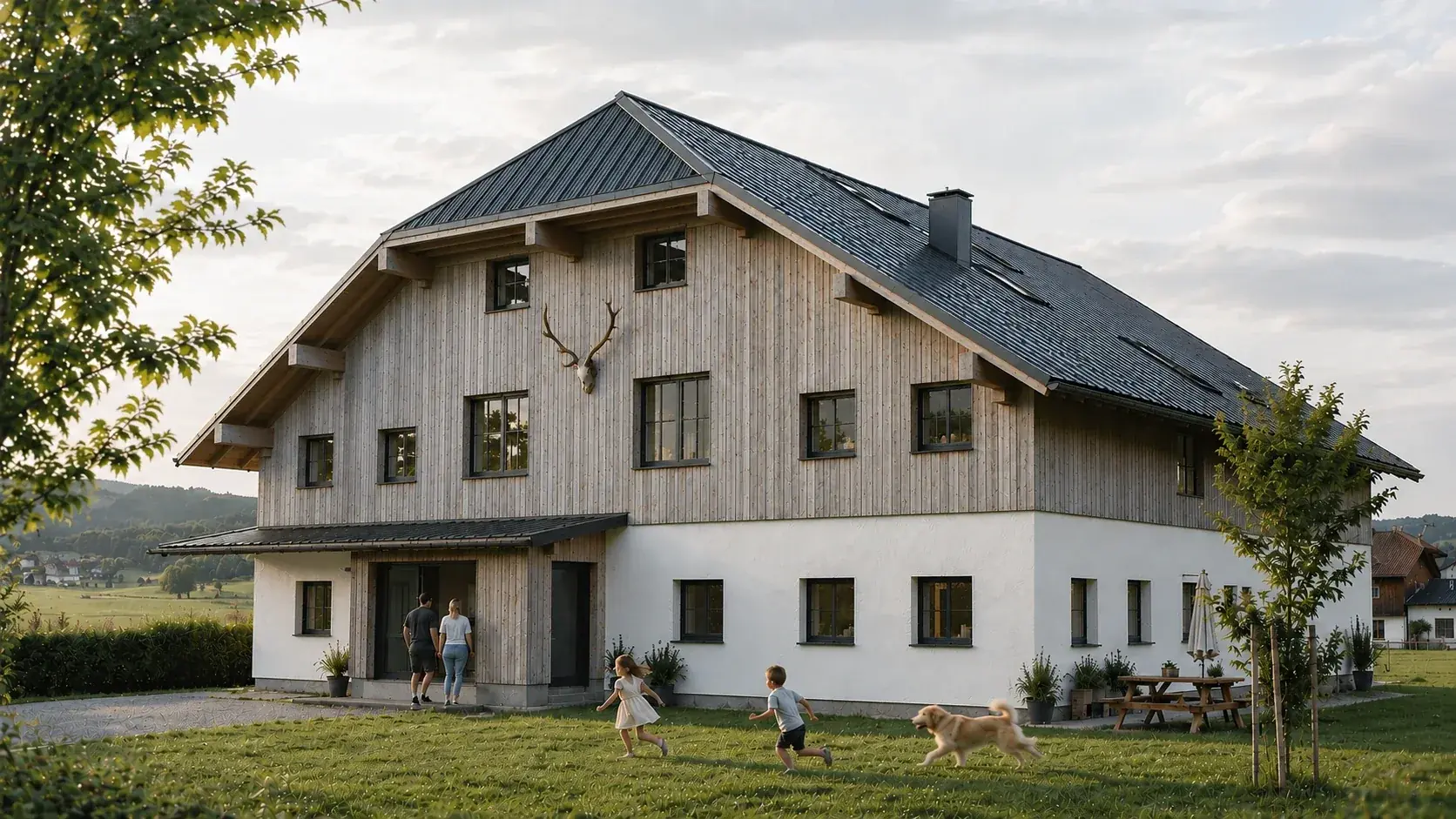 Haus WODO – Bauernhaus mit weiß verputztem Sockel, silbergrauer Holzschalung im Obergeschoss und dunklem Satteldach