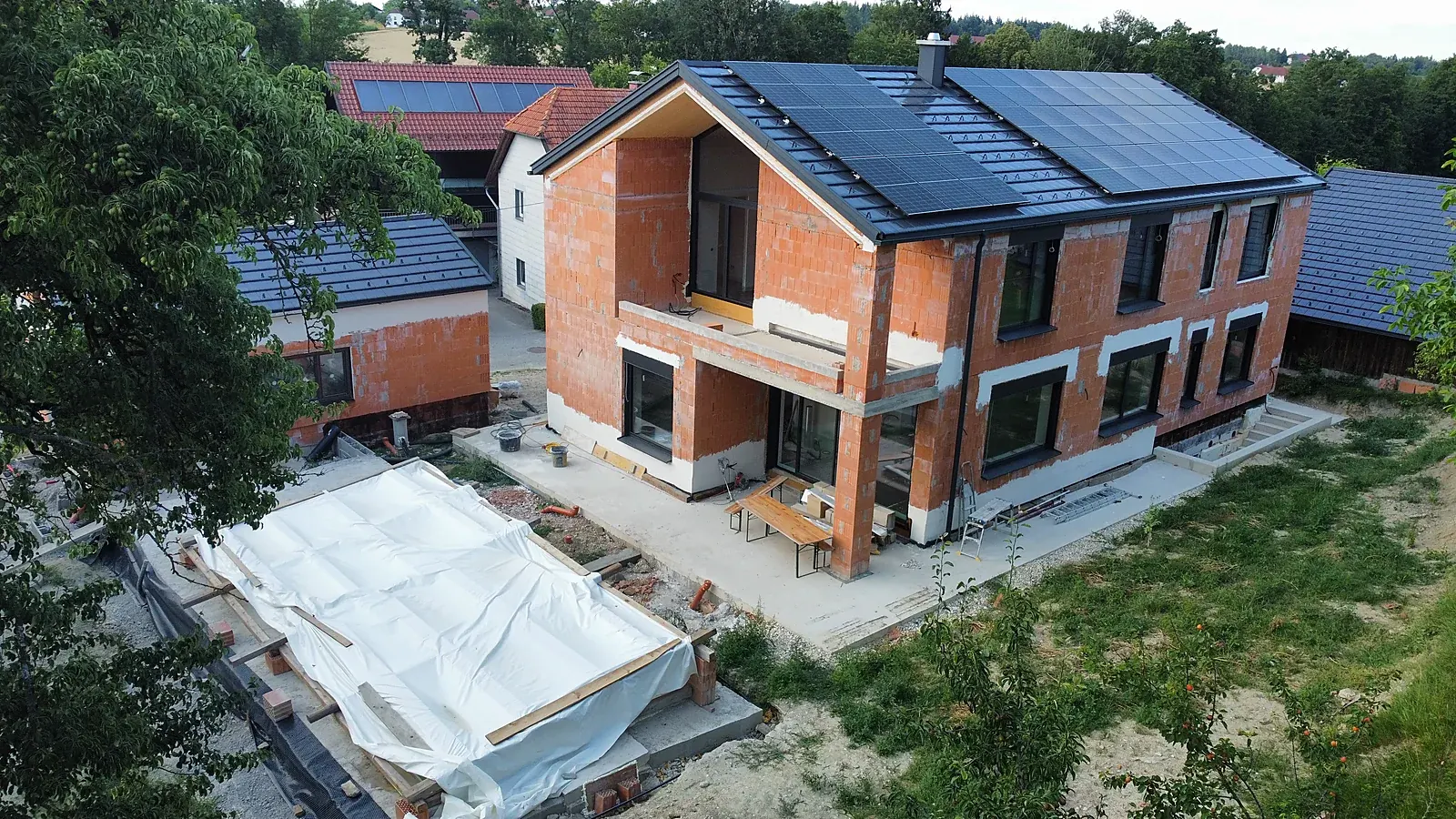 Luftaufnahme des Hauses ZEWI im Rohbau – Satteldach mit PV-Anlage, Terrasse und Garten